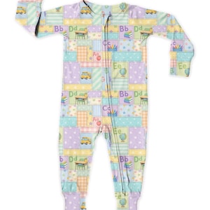May include: A pastel-coloured baby sleepsuit with a patchwork design. The pattern includes school-related motifs such as apples, school buses, globes, and letters. The colour scheme features soft blues, greens, yellows, and purples.