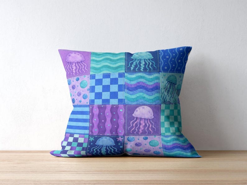 May include: Square cushion with a patchwork design featuring jellyfish, waves, and geometric patterns in shades of blue, purple, and teal. The cushion is placed on a wooden surface.