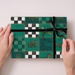 May include: A wrapped gift with a green and black dinosaur pattern. The gift is decorated with a black ribbon and bow. The wrapping paper features a patchwork design with various dinosaur illustrations and checkered squares.
