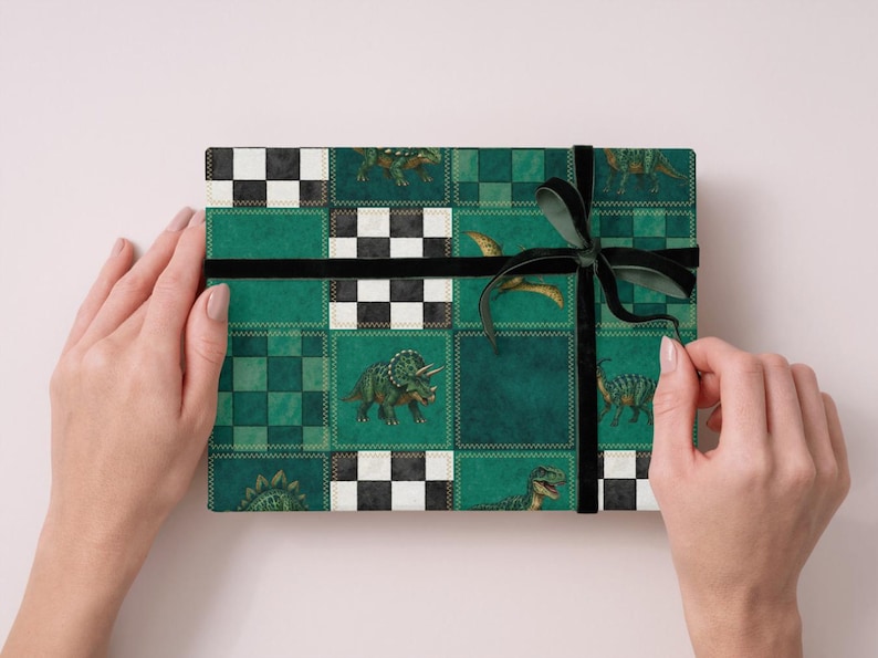 May include: A wrapped gift with a green and black dinosaur pattern. The gift is decorated with a black ribbon and bow. The wrapping paper features a patchwork design with various dinosaur illustrations and checkered squares.