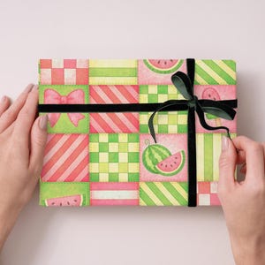 May include: A gift box wrapped in colorful paper with a watermelon pattern. The paper features a patchwork design with pink, green, and yellow squares, and is tied with a black ribbon and bow.
