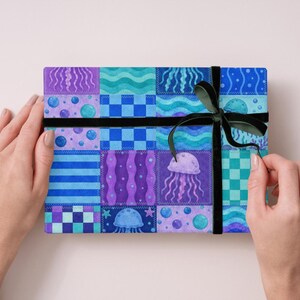 May include: A rectangular gift box wrapped in patterned paper with a black ribbon and bow. The paper features a patchwork design with blue, purple, and teal squares, including jellyfish and bubble motifs.