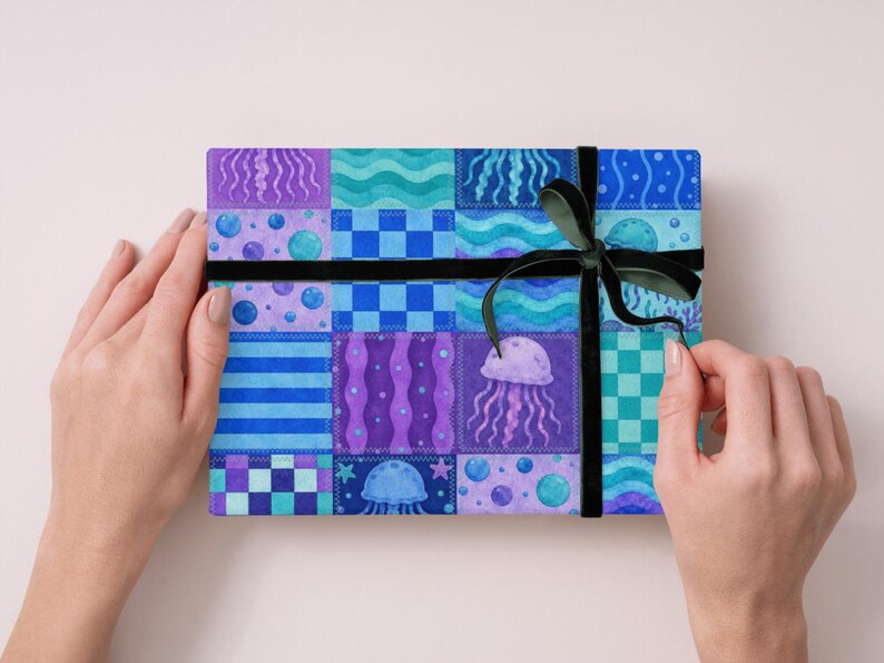 May include: A rectangular gift box wrapped in patterned paper with a black ribbon and bow. The paper features a patchwork design with blue, purple, and teal squares, including jellyfish and bubble motifs.