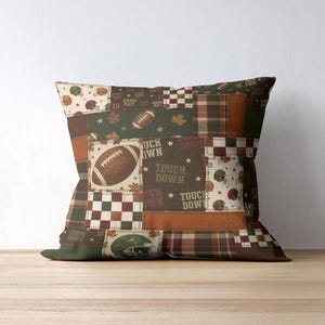 May include: Square decorative pillow with a patchwork design featuring footballs, helmets, and the words "Touch Down" on a brown, green, and orange background. The pillow has a plaid pattern and a solid green border.