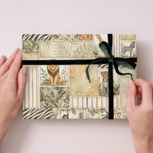 May include: A rectangular gift box with a safari animal print design, featuring a lion, zebra, and giraffe. The box is wrapped with a black ribbon and a dark green bow. The box is held by two hands.