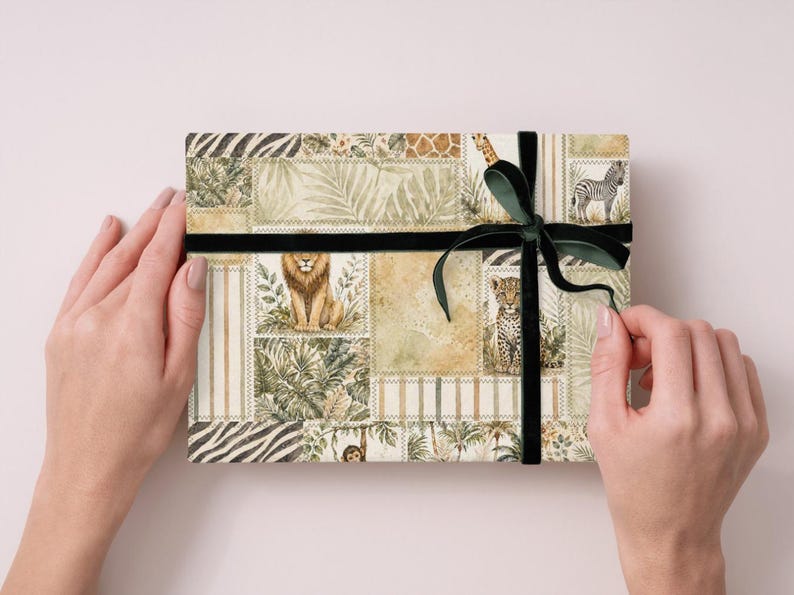 May include: A rectangular gift box with a safari animal print design, featuring a lion, zebra, and giraffe. The box is wrapped with a black ribbon and a dark green bow. The box is held by two hands.