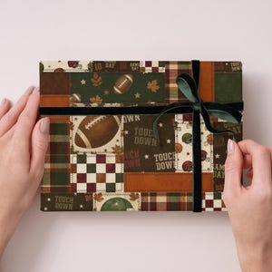 May include: A wrapped gift box with a football-themed patchwork design. The box features a dark green ribbon and bow. The patchwork includes footballs, leaves, and the words "Touch Down" in a mix of brown, green, and cream colors.
