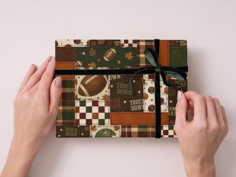 May include: A wrapped gift box with a football-themed patchwork design. The box features a dark green ribbon and bow. The patchwork includes footballs, leaves, and the words "Touch Down" in a mix of brown, green, and cream colors.