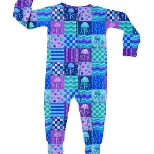 May include: A patterned sleepsuit in a patchwork design. The all-in-one garment features a repeating pattern of jellyfish, wavy lines, and polka dots in blue, purple, and teal. The sleepsuit has a zip down the front.