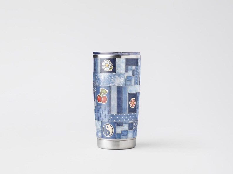 Op de afbeelding: Een roestvrijstalen beker met een patchwork denim design. De beker heeft verschillende patches met een madeliefje, kersen, een bloem en een yin-yang symbool. De beker is ongeveer 18 cm hoog.