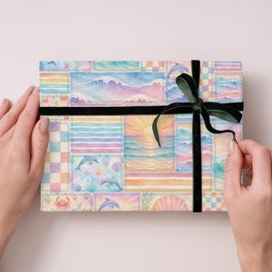 Pode incluir: Uma caixa de presente retangular embrulhada em papel aquarela colorido com cenas oce&acirc;nicas, golfinhos e um p&ocirc;r do sol. A caixa &eacute; amarrada com uma fita de veludo preta e um la&ccedil;o verde escuro.