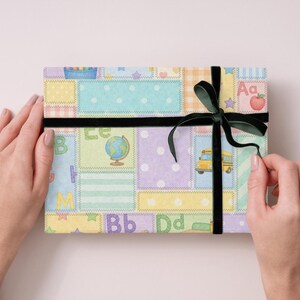 May include: A present wrapped in paper with a patchwork design featuring school-themed illustrations. The gift is tied with a black velvet ribbon and bow. The illustrations include a school bus, globe, and apple.
