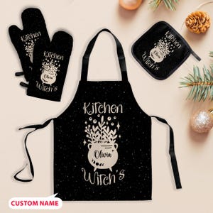 May include: A black kitchen set including an apron, oven mitts, and a pot holder. Each item features a white design of a cauldron with the text "Kitchen" and "Olivia Witch's". The apron and pot holder have a black background with white speckles.