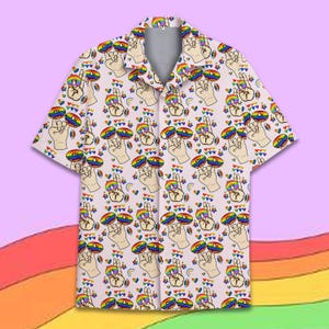 May include: Short-sleeved button-up shirt with a repeating pattern of hands making the peace sign, rainbow-colored donuts, hearts, and rainbows on a light pink background. The shirt has a collared neckline and a relaxed fit.