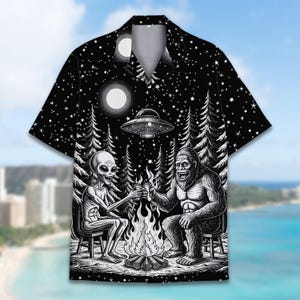 Könnte beinhalten: Schwarzes kurzärmeliges Hemd mit einer einzigartigen Grafik. Das Design zeigt einen Außerirdischen und Bigfoot, die sich um ein Lagerfeuer unter einem Sternenhimmel zuprosten, mit einem UFO darüber. Das Hemd hat einen klassischen Kragen und eine lockere Passform.