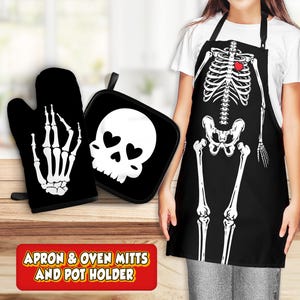 Op de afbeelding: Zwarte schort met een wit skeletontwerp en een rood hart. De schort wordt geleverd met zwarte ovenwantjes en een pannenlappen met een witte schedel met harten als ogen. De tekst "Apron & Oven Mitts and Pot Holder" is gedrukt op een rode banner.
