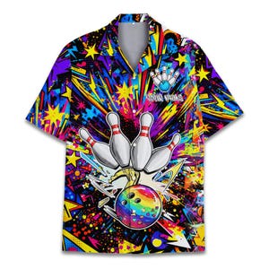 Puede incluir: Camisa de bolos de manga corta con un diseño vibrante y colorido. La camisa presenta un gráfico de bola y bolos de bolos con una bola de color arcoíris. El fondo es una mezcla de amarillo, morado y azul con formas de estrella y rayo.