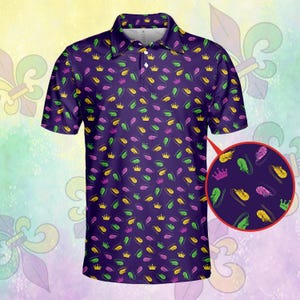 May include: Purple polo shirt with a pattern of gold crowns and green, yellow, and purple feathers. The shirt has a classic collar and a three-button placket. A close-up shows the pattern details.
