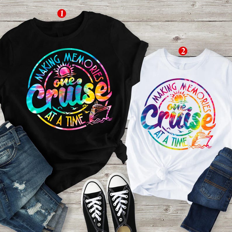 May include: Two t-shirts, one black and one white, with a colourful tie-dye design. Each shirt features a circular graphic with the text "Making Memories One Cruise At A Time" and a cruise ship illustration. Paired with jeans and black trainers.
