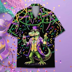 May include: Black button-up shirt featuring a cartoon alligator in a purple coat, top hat, and bow tie, holding a wine glass and a bottle. The shirt has a Mardi Gras theme with beads and confetti.