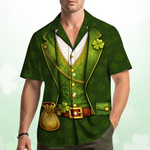 May include: Green short-sleeved shirt featuring a printed design of a green suit jacket, vest, and gold chain. The design includes a brown belt with a gold buckle, a small pouch, and a shamrock. The shirt has a white collared shirt design.