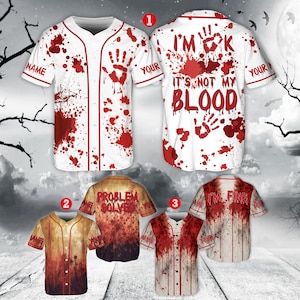 May include: White baseball jersey with red blood splatter and handprints. The front says "NAME" and "YOUR" on the sleeves. The back says "I'M OK IT'S NOT MY BLOOD". Other jerseys have "PROBLEM SOLVED" and "I'M FINE".
