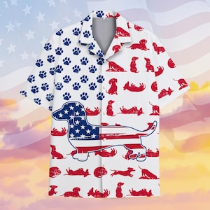 Op de afbeelding: Wit overhemd met knopen met een patriottisch thema. De linkerkant heeft blauwe pootafdrukken, terwijl de rechterkant rode teckel silhouetten heeft. Een teckel omtrek gevuld met het Amerikaanse vlagontwerp staat op de voorkant.