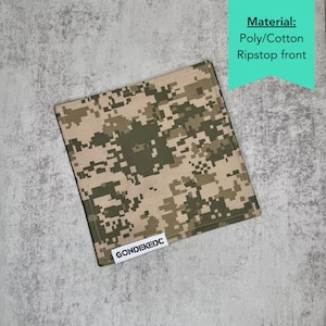 May include: A square-shaped handkerchief featuring a digital camouflage pattern in shades of tan, olive green, and dark brown. The fabric is a poly/cotton ripstop material. A small white rectangular tag with the black text GONDEKEDC is sewn on.
