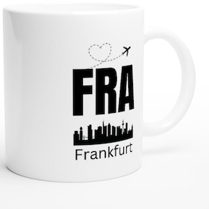 Könnte beinhalten: Weiße Keramiktasse mit einer schwarzen Silhouette der Frankfurter Skyline und dem Text "FRA Frankfurt" mit einem Herz und einem Flugzeug-Motiv.