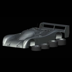 May include: A silver model racing car with a large rear wing and four detached black tyres. The car has a sleek, aerodynamic design, with a low profile and a cockpit. The background is solid black.