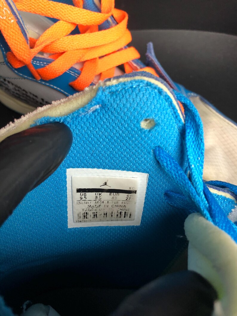 K&ouml;nnte beinhalten: Nahaufnahme eines blau-wei&szlig;en Sneakers mit orangefarbenen Schn&uuml;rsenkeln. Das Innere des Schuhs ist hellblau, mit einem wei&szlig;en Etikett mit Markenname und Gr&ouml;&szlig;enangaben. Der Schuh wird in China hergestellt.