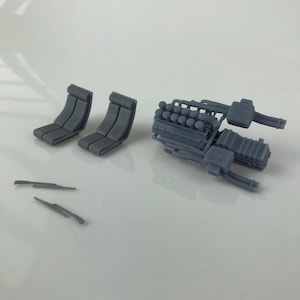 May include: A set of gray plastic model car parts, including two seats, two windshield wipers, and a detailed engine with pipes and cylinders.