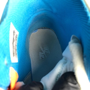 K&ouml;nnte beinhalten: Innenansicht eines High-Top-Sneakers. Das Innere des Schuhs hat ein leuchtend blaues Futter und eine hellgraue Innensohle. Die Innensohle hat ein Logo. Das Design des Schuhs ist sichtbar und zeigt die Materialien und die Konstruktion.