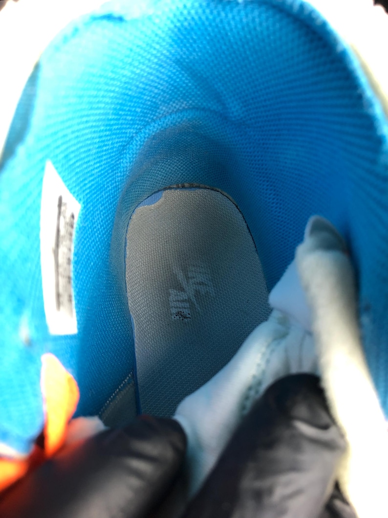 K&ouml;nnte beinhalten: Innenansicht eines High-Top-Sneakers. Das Innere des Schuhs hat ein leuchtend blaues Futter und eine hellgraue Innensohle. Die Innensohle hat ein Logo. Das Design des Schuhs ist sichtbar und zeigt die Materialien und die Konstruktion.