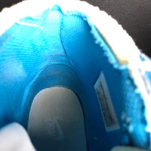 K&ouml;nnte beinhalten: Innenansicht eines blau-wei&szlig;en Sneakers. Der Innenraum hat ein hellblaues Stofffutter und eine wei&szlig;e Innensohle. Die &Ouml;ffnung des Schuhs ist mit wei&szlig;em Material eingefasst. Ein Etikett ist an der Seite sichtbar.