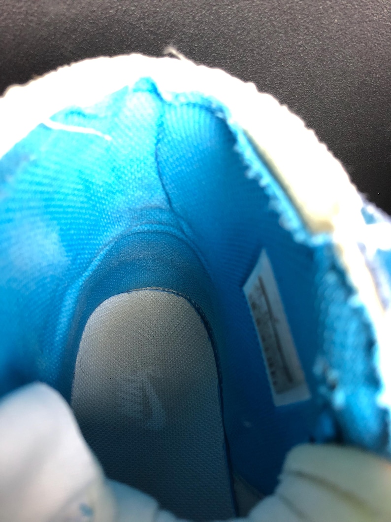 K&ouml;nnte beinhalten: Innenansicht eines blau-wei&szlig;en Sneakers. Der Innenraum hat ein hellblaues Stofffutter und eine wei&szlig;e Innensohle. Die &Ouml;ffnung des Schuhs ist mit wei&szlig;em Material eingefasst. Ein Etikett ist an der Seite sichtbar.
