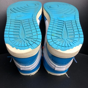 K&ouml;nnte beinhalten: Paar blaue und wei&szlig;e Turnschuhe mit hellblauen Sohlen. Die Sohlen haben ein strukturiertes Muster und das Nike-Logo. Die Schuhe haben blaue Schn&uuml;rsenkel und wei&szlig;e Akzente.