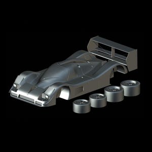 Op de afbeelding: Een zilverkleurig model van een raceauto met losse wielen en een achtervleugel, tegen een zwarte achtergrond. De carrosserie van de auto heeft een gestroomlijnd ontwerp met koplampen en een cockpit. De wielen zijn los.