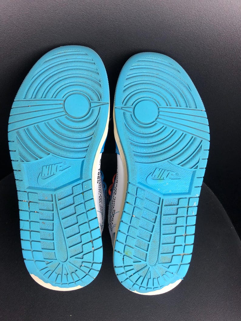 K&ouml;nnte beinhalten: Paar Turnschuhe mit hellblauen Sohlen. Die Sohlen haben ein strukturiertes Muster und das Nike-Logo. Die Oberteile sind wei&szlig; mit blauen und orangefarbenen Akzenten. Die Schuhe sind f&uuml;r sportliche Aktivit&auml;ten konzipiert.