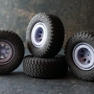 Könnte beinhalten: Vier schwarze Reifen aus Gummi mit weißen Felgen. Die Reifen haben ein Profil und sind für den Offroad-Einsatz konzipiert.