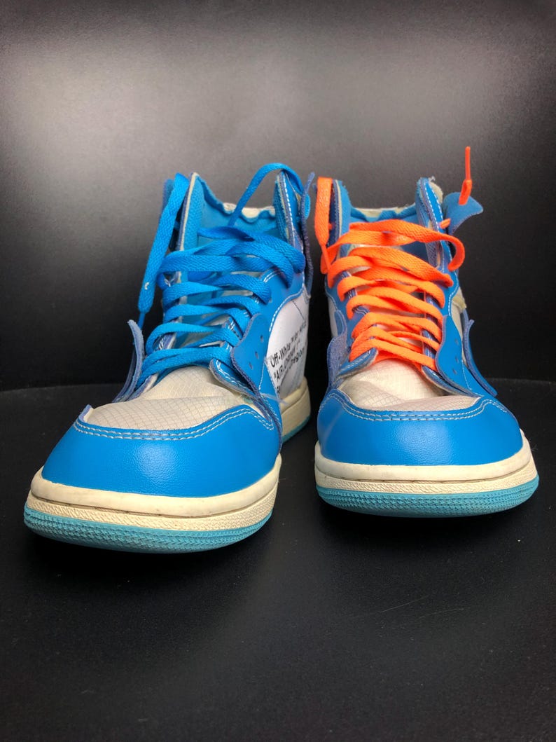 K&ouml;nnte beinhalten: Paar High-Top-Sneaker mit blau-wei&szlig;en Paneelen, mit blauen und orangefarbenen Schn&uuml;rsenkeln. Die Schuhe haben eine hellblaue Sohle und eine wei&szlig;e Mesh-Zunge. Das Design enth&auml;lt Text auf der Seite.