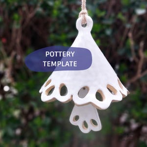 May include: White ceramic bell-shaped pottery with a scalloped edge and circular cutouts. The bell is suspended by a natural fiber rope. The text "POTTERY TEMPLATE" is displayed on a blue oval.