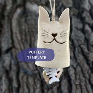 May include: A cream-colored ceramic cat-shaped wind chime hanging from a jute string. The cat has pointed ears, etched whiskers, and a cutout nose and mouth. A white ceramic fish skeleton clapper hangs from the bottom. Text reads POTTERY TEMPLATE.