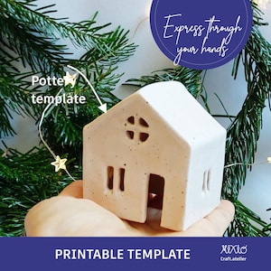 May include: Printable template for a white ceramic house with a window and a door. The template is on a hand against a background of green pine branches and white lights.