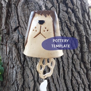 May include: A ceramic wind chime shaped like a dog head with brown ears, a black nose, and a paw print clapper hanging below. The piece features a cream-colored glaze with dark speckles and a purple oval overlay with the text POTTERY TEMPLATE.