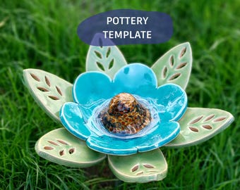 May include: A ceramic flower sculpture featuring light green leaves with cut-out details and a bright turquoise petal layer. The centre is a raised, textured brown and gold dome. The text POTTERY TEMPLATE is visible above the object.