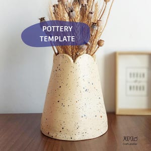May include: A speckled beige ceramic vase with a scalloped rim, holding dried wheat and seed pods. The vase has blue and brown speckles. Text on a blue oval reads "POTTERY TEMPLATE".