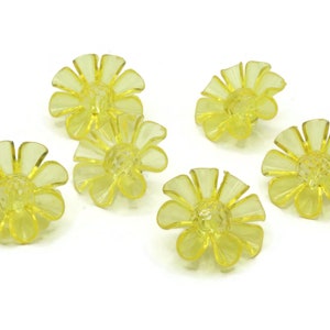 Op de afbeelding: Zes gele plastic bloemvormige ornamenten. De ornamenten hebben een gekrulde rand en een klein gaatje in het midden.