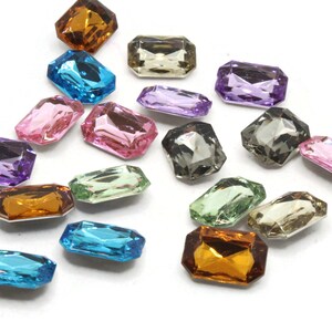 May include: Assortment of colorful, faceted, rectangular glass gems. The gems are in various shades of blue, green, purple, pink, brown, and gray.