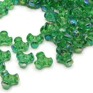 Könnte beinhalten: Nahaufnahme eines Haufens grüner, irisierender Glasperlen. Die Perlen haben die Form eines dreiblättrigen Kleeblatts und eine glänzende, reflektierende Oberfläche.